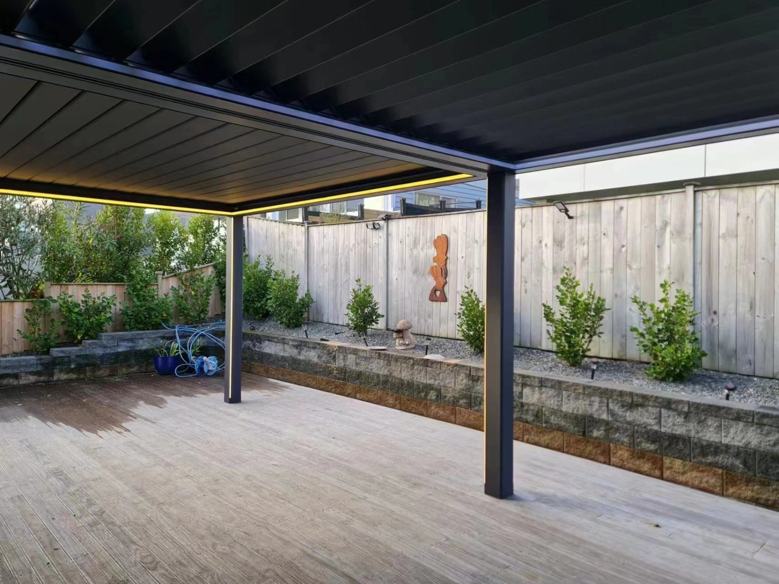 Dark pergola frame above a garden deck — aluminium pergola